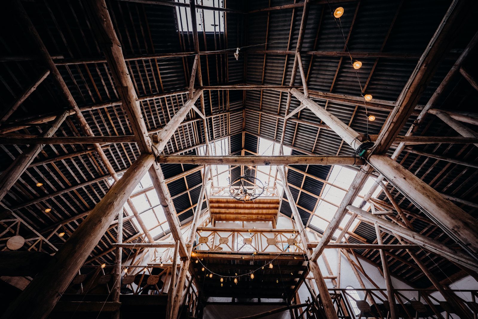 A dramatic view inside a rustic barn showcasing wooden beams and steel framework.