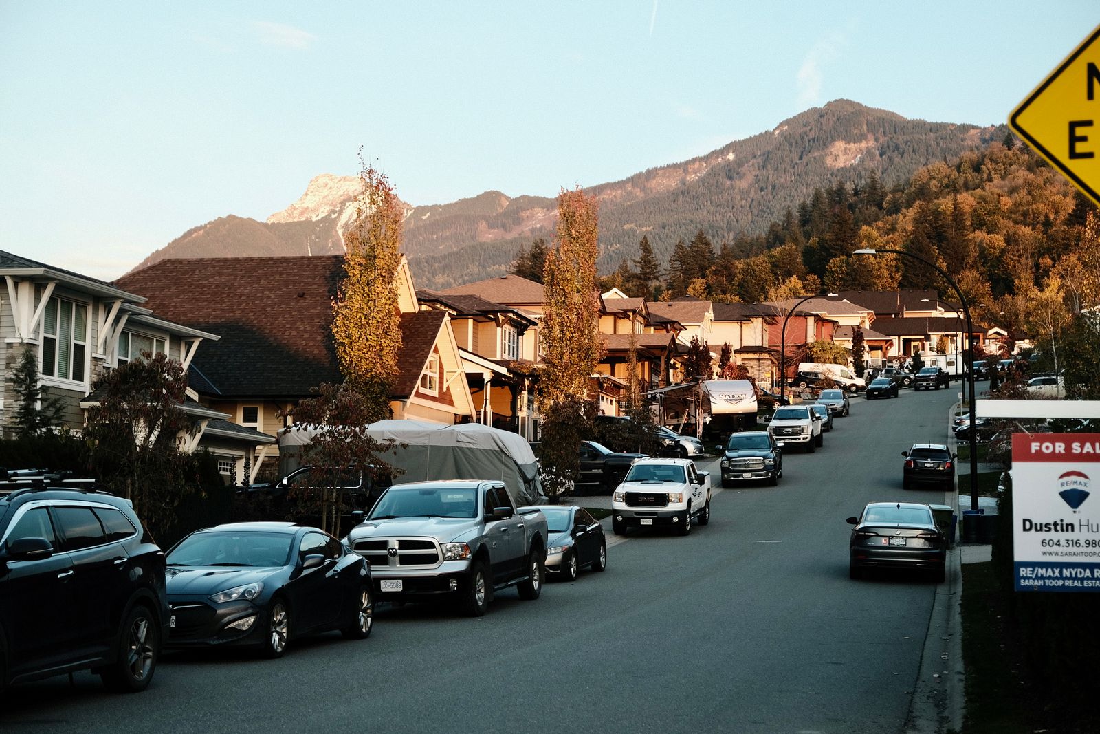 A serene suburban street lined with cars and mountain views under clear skies.