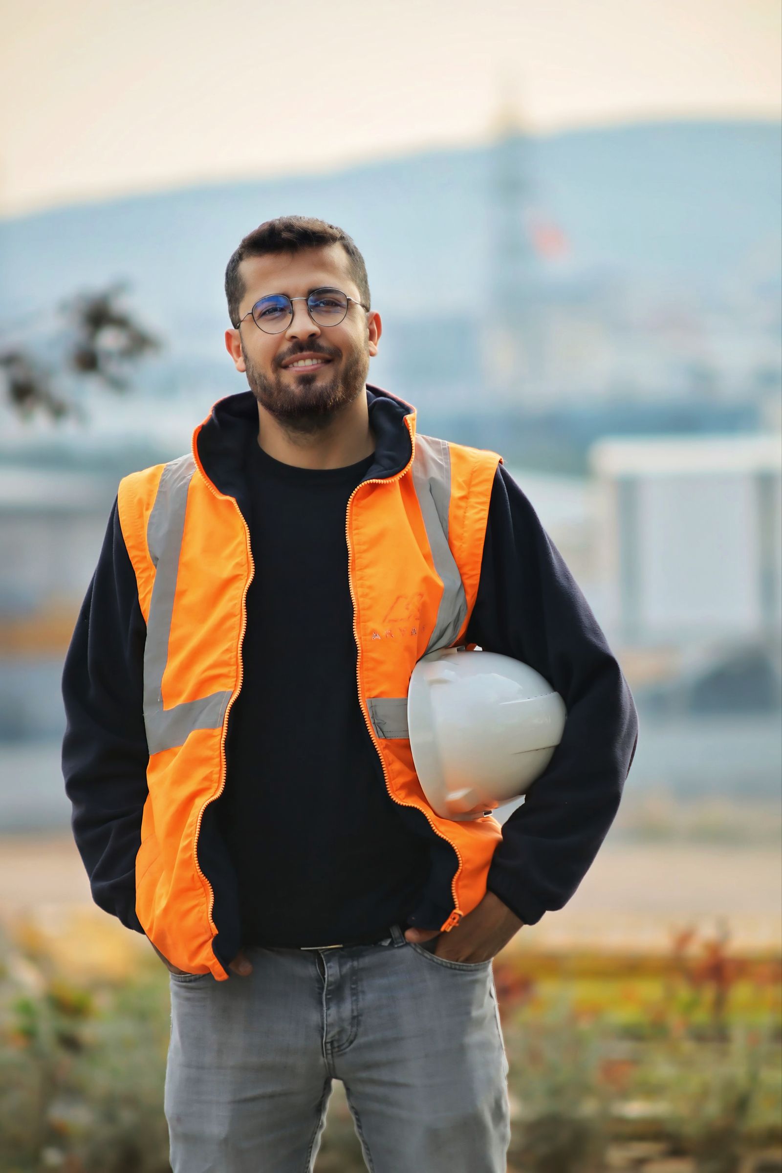 Confident male construction worker with safety vest and hard hat in a blurred outdoor setting.