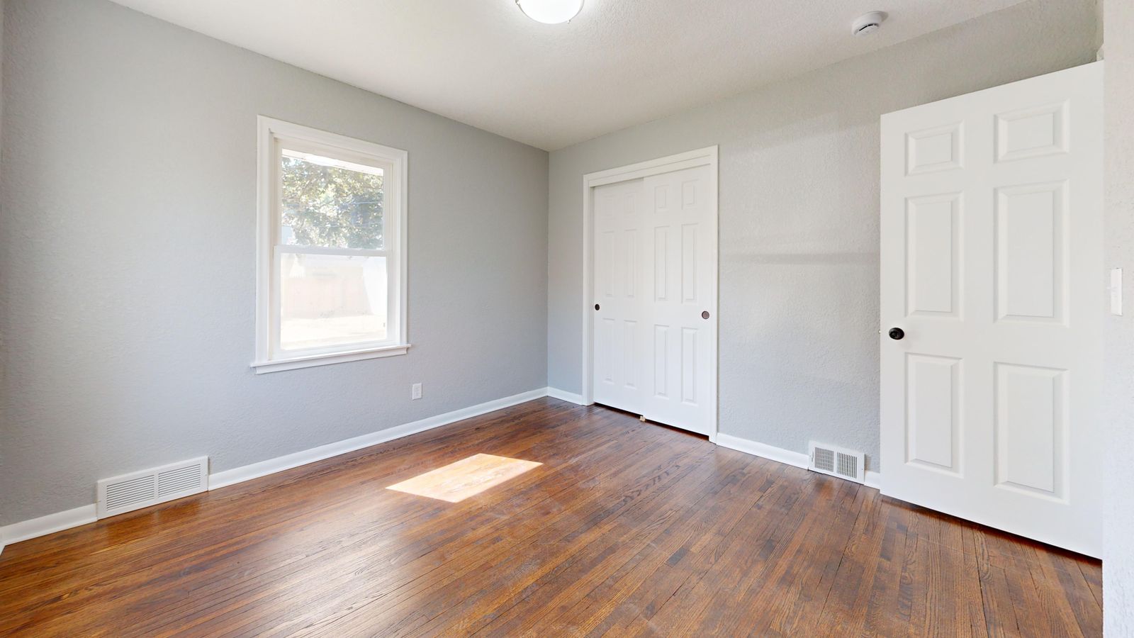Spacious empty room with hardwood floors and sunlight streaming through the window.