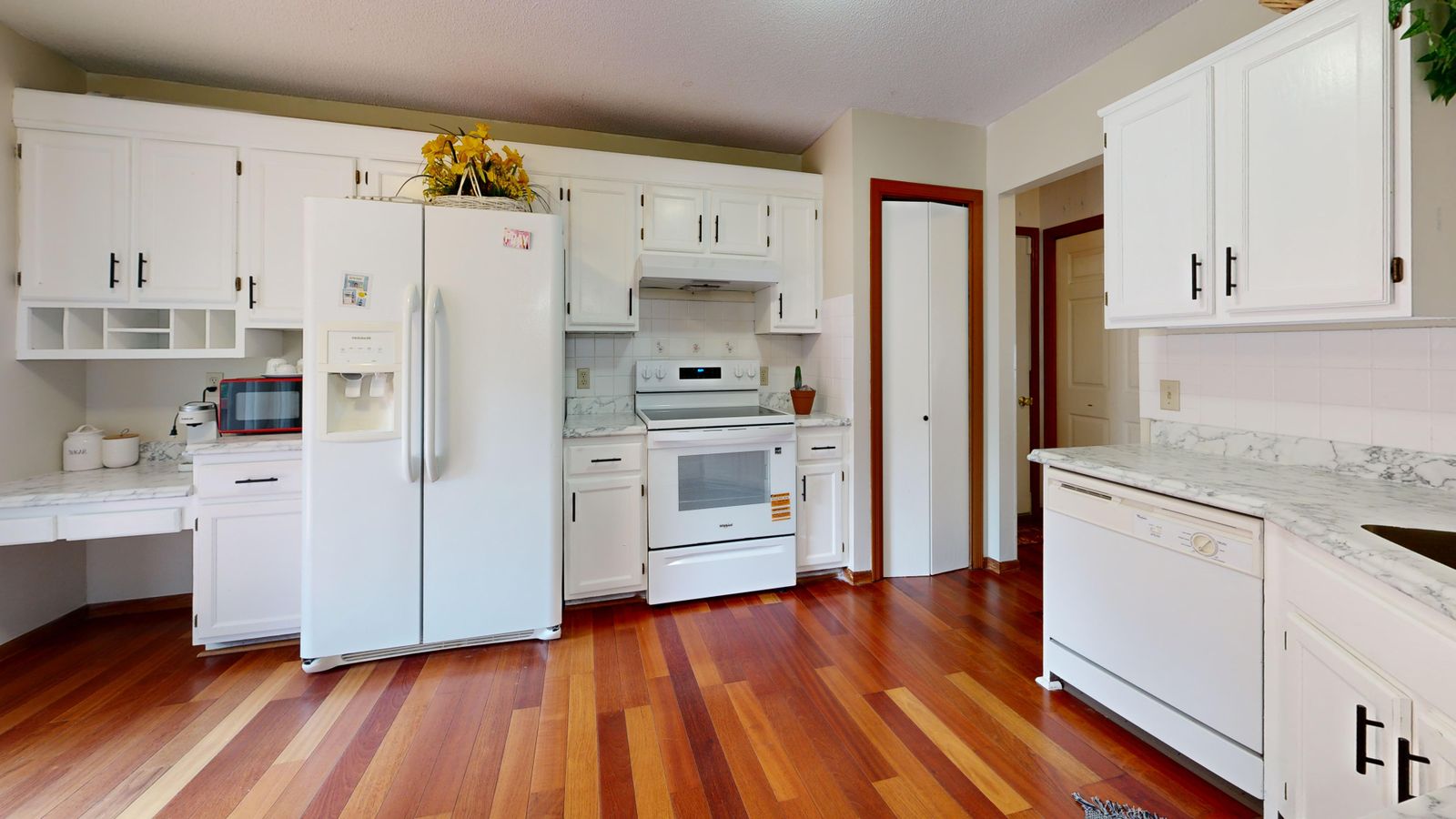 Bright kitchen featuring white cabinets and appliances with hardwood floors.