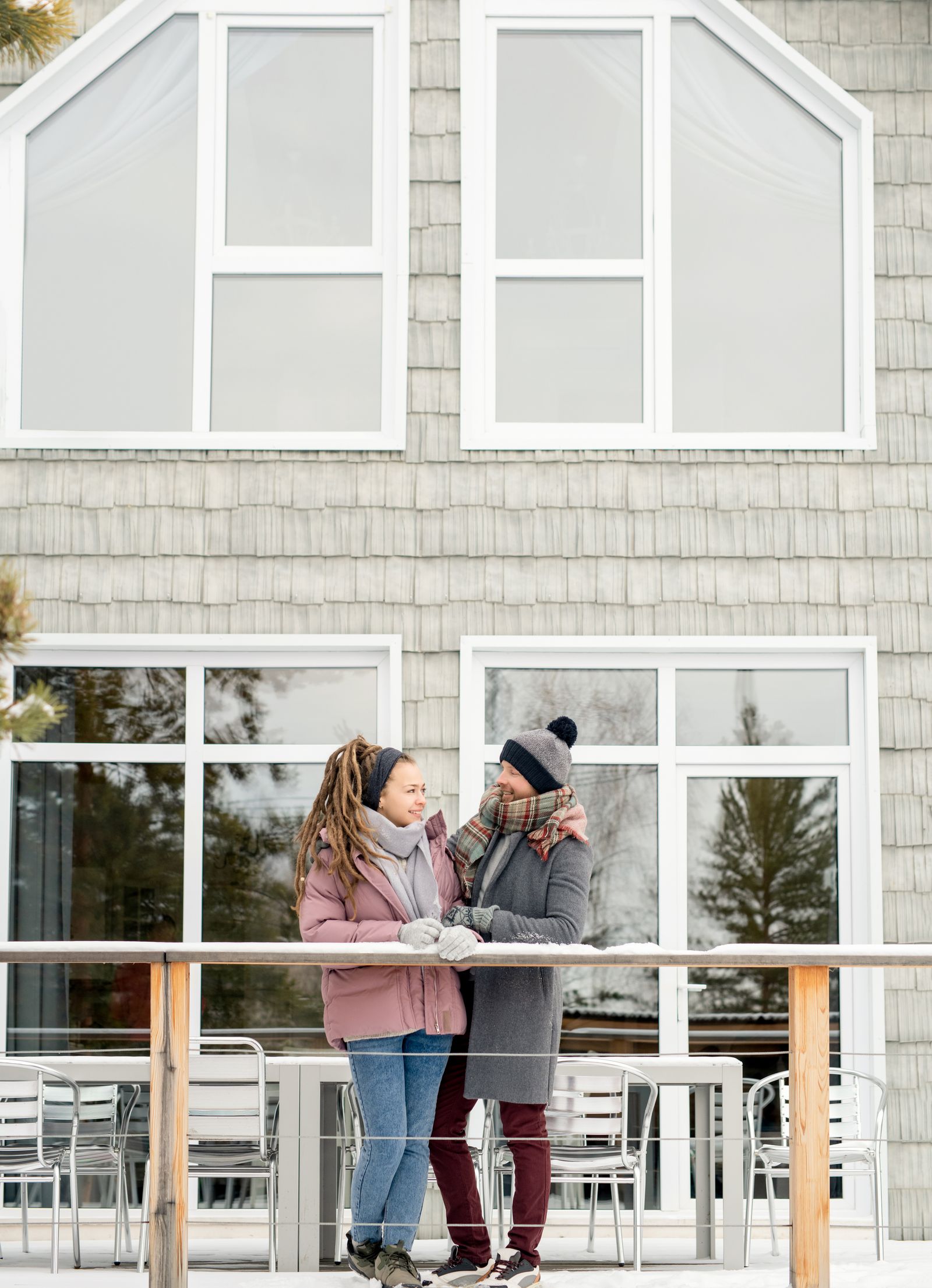 Couple warmly dressed enjoying winter scenery from modern balcony. Capturing love and architecture.