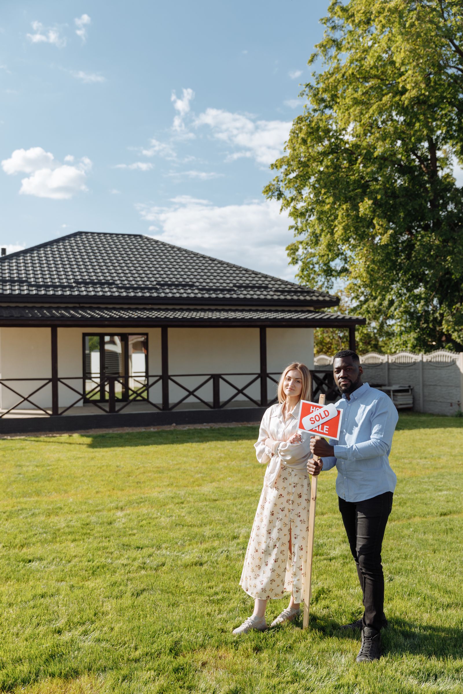 Diverse couple celebrating new home purchase with a sold sign outdoors.